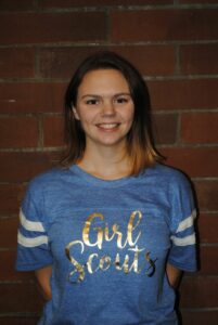 Girl Scout alum Molly Carle smiling, wearing a blue Girl Scout shirt.