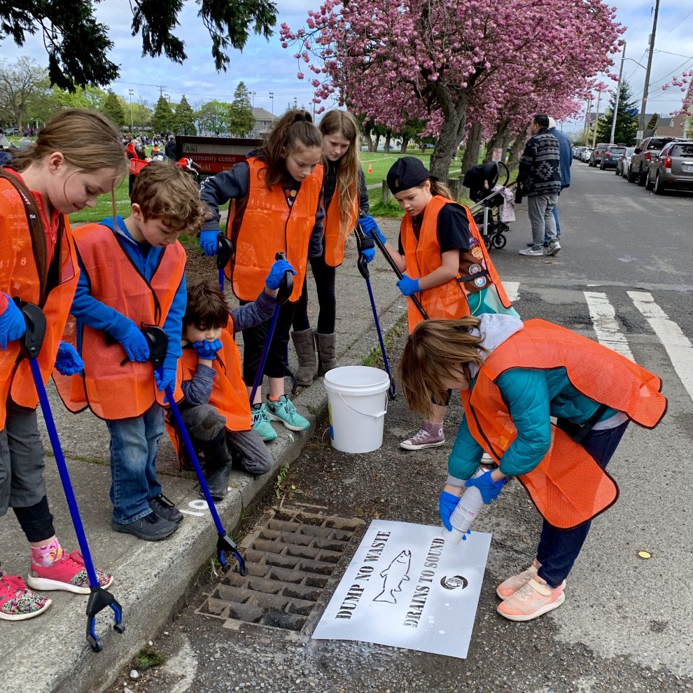Girl Scouts of Western Washington troop cleans up sidewalk and spray painting a sign saying dump no waste drains to sound
